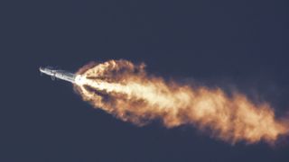 flames shoot from the bottom of a sliver rocket as it rises into a dark blue sky.