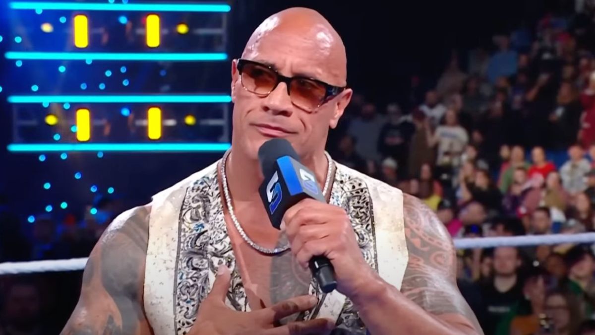 Dwayne Johnson staring at the New Orleans crowd while wearing sunglasses and holding a microphone.