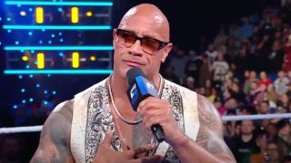 Dwayne Johnson staring at the New Orleans crowd while wearing sunglasses and holding a microphone.