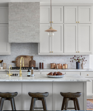 A white and cream-toned kitchen with a gold faucet and brown bar stools