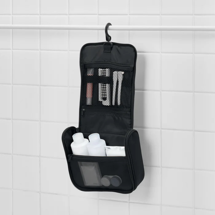 A black hanging toiletry case by Muji against a white tile wall