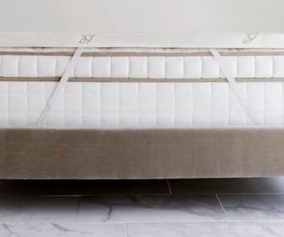 The Saatva Graphite Mattress Topper on a mattress on marble floor.