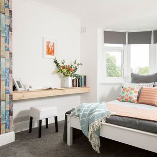 teen bedroom has white walls with white windows grey bed and shelf containing books.