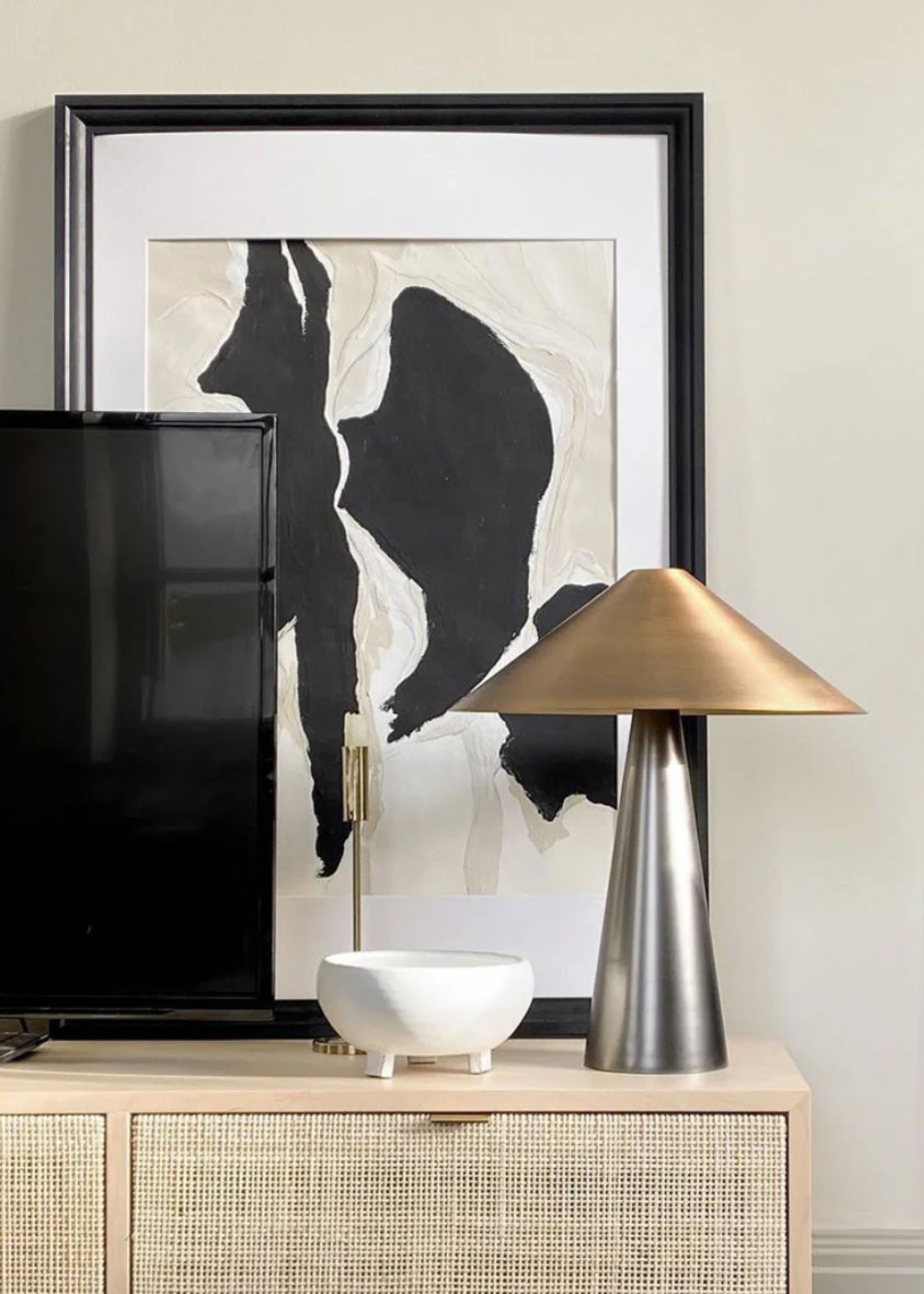 A gold and silver lamp on top of a console beside a TV console and artwork