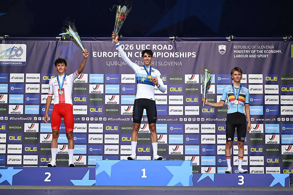 Three riders on a podium with steps in dark blue with lighter blue stars and a busy backdrop with advertisers