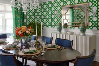 oval dark wood dining table set with bright flowers and blue chairs with green trellis wallpaper behind