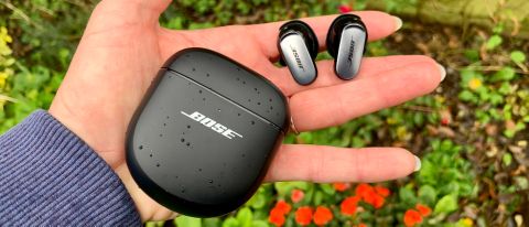 Bose QuietComfort Ultra oordopjes in een hand met de case, boven een bloembed.