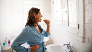 Top mistakes when brushing your teeth - Woman brushing teeth in bathroom mirror