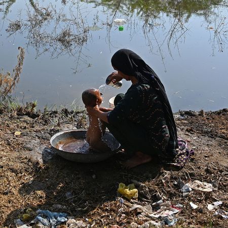 An internally displaced flood-affected woman bathes her child at a makeshift camp in Mehar city after heavy monsoon rains in Dadu district, Sindh province on September 9, 2022. - Record monsoon rains have caused devastating floods across Pakistan since June, killing more than 1,200 people and leaving almost a third of the country under water, affecting the lives of 33 million