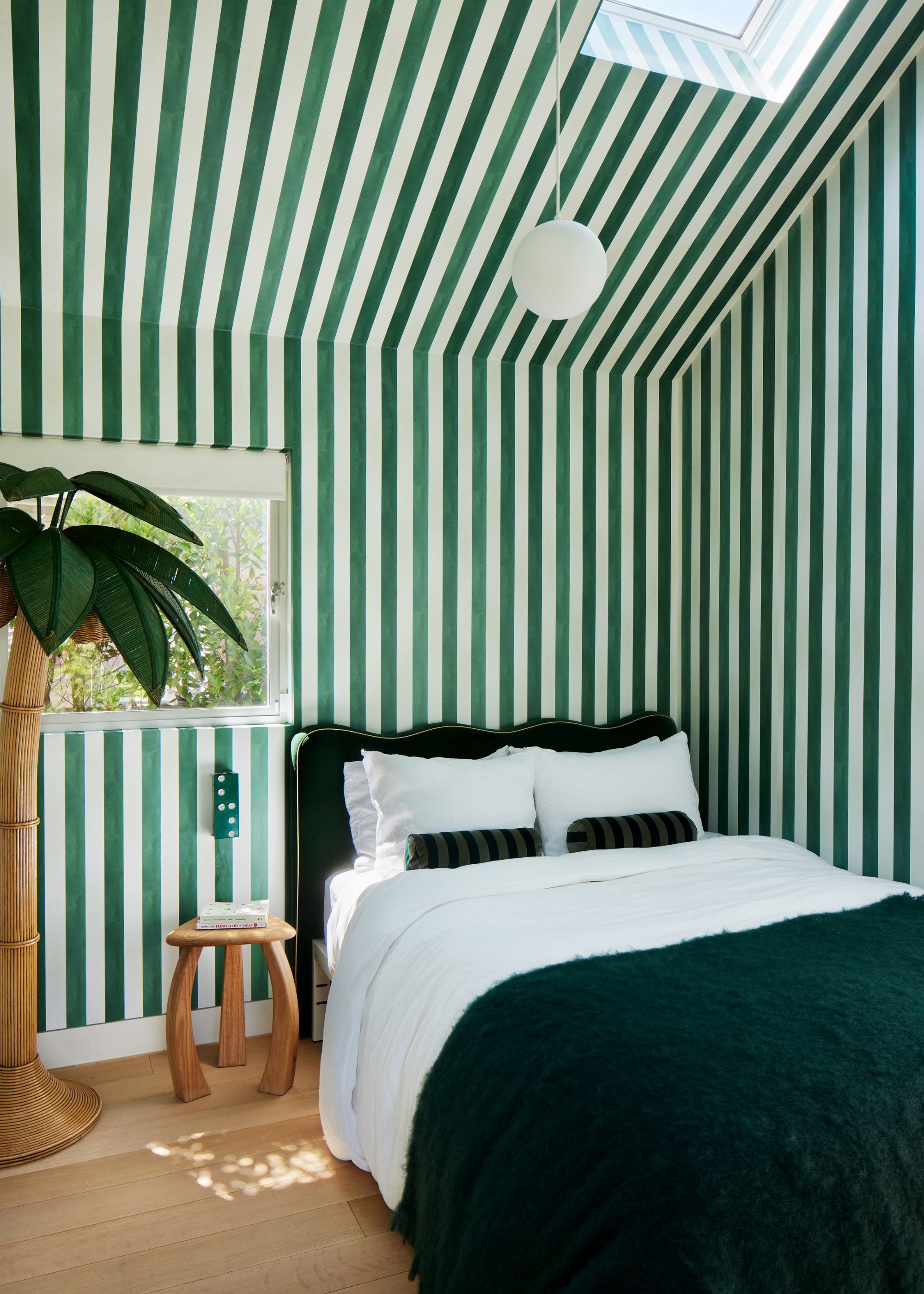 A modern bedroom with green and white striped wallpaper on all walls and a sloped ceiling.
