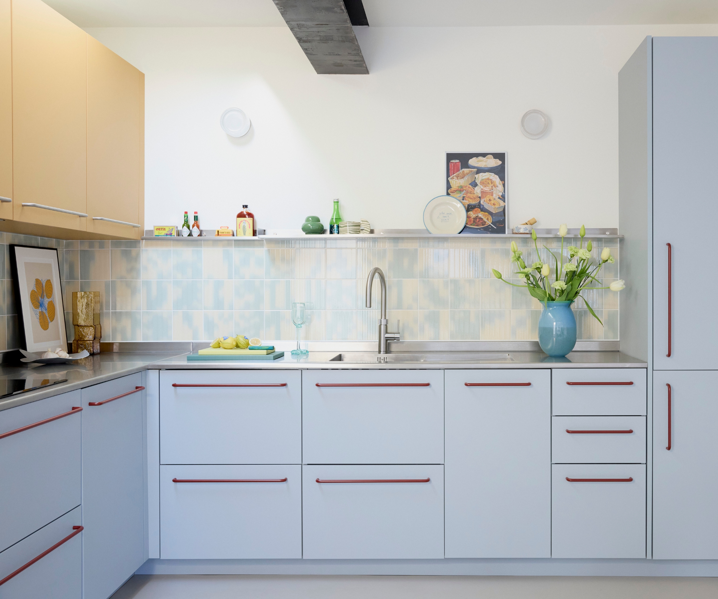 An L-shaped kitchen with light blue MDF cabinets, white walls, and a blue and white tile backsplash