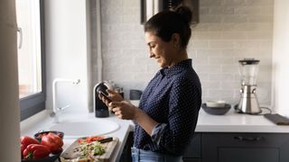 Woman looks at phone in front of chopping board in kitchen