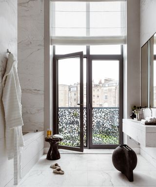 marble bathroom with metal doors, large mirror and small black occasional table