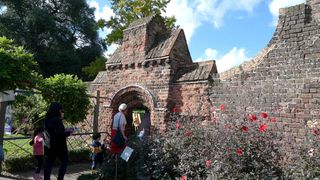 Children pass through an arch with red dahlias in the walled garden at Fulham Palace, London