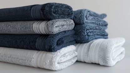 Blue, white and gray towels stacked on top of each other in front of a gray background.