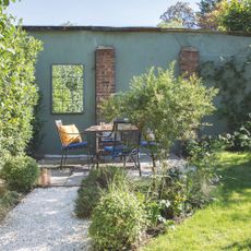 Gravel path through the garden leading to a seating area with table and chairs beside a green wall. Garden redesign of a small city garden in London, owned by Rosie Money-Coutts.