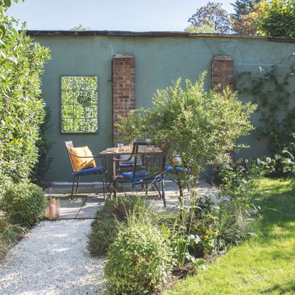 Gravel path through the garden leading to a seating area with table and chairs beside a green wall. Garden redesign of a small city garden in London, owned by Rosie Money-Coutts.