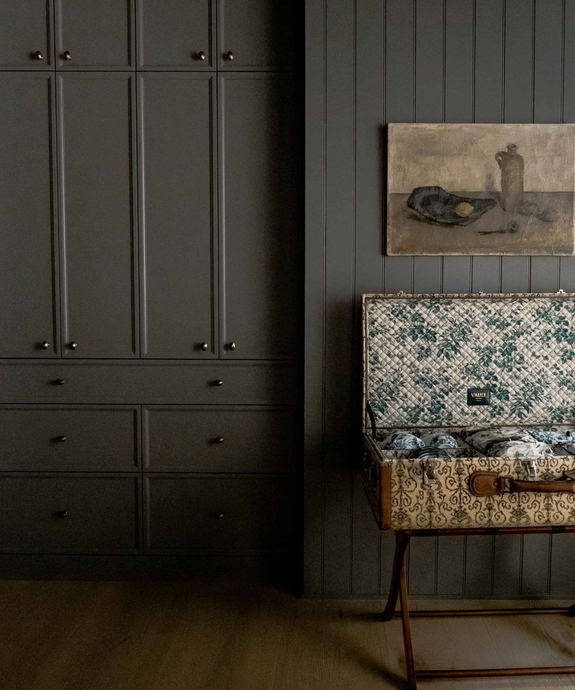 a wall of built-in cabinets painted in dark gray and a vintage luggage basket open on a luggage holder