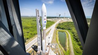 a brown and white rocket rolls vertically toward its launch pad beneath a blue sky