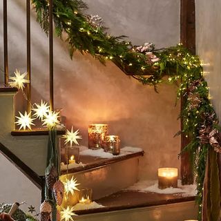 Faux cedar garland wrapped around a staircase with candles and star lights