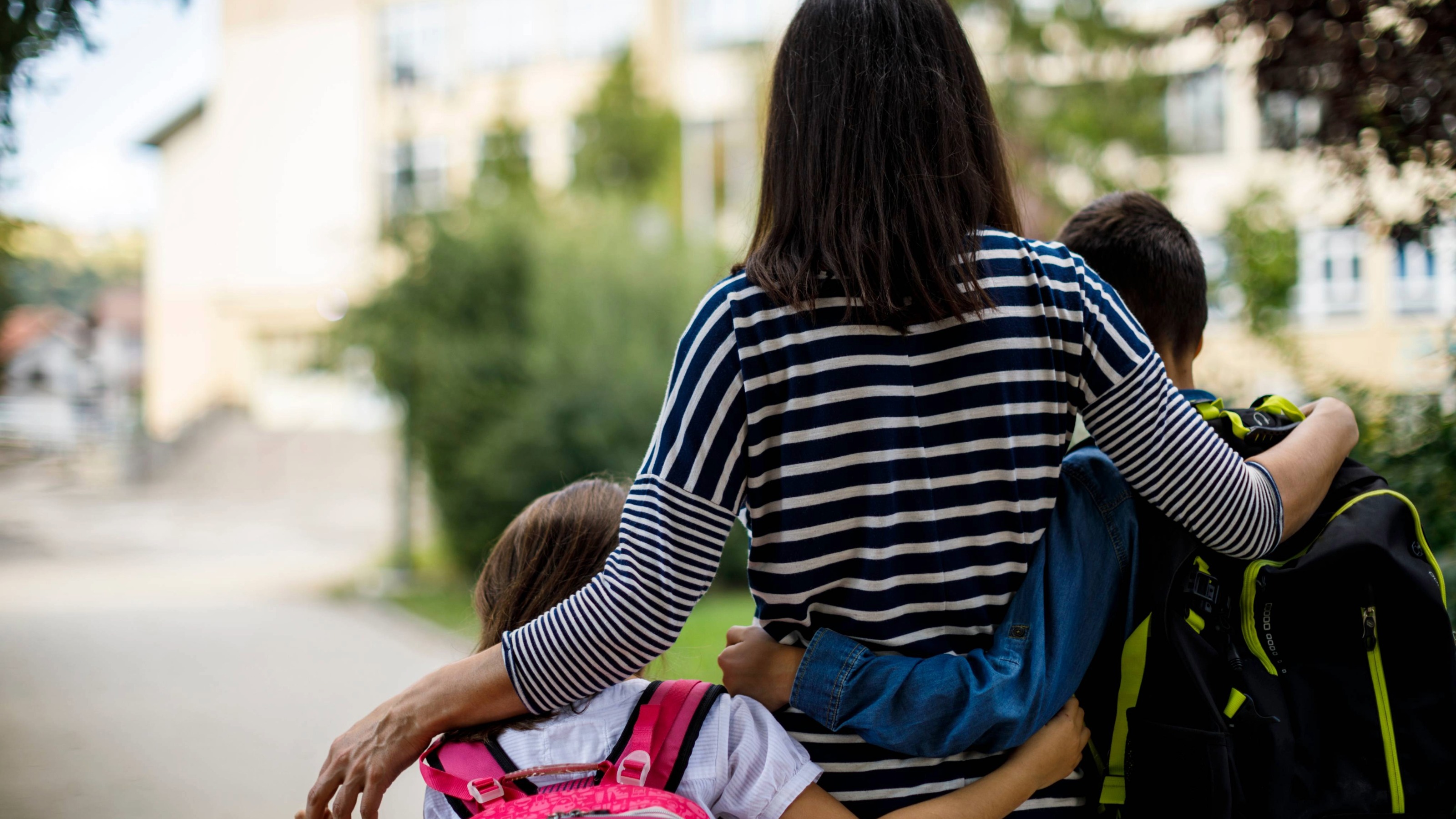 Rear view of mother taking two kids to school