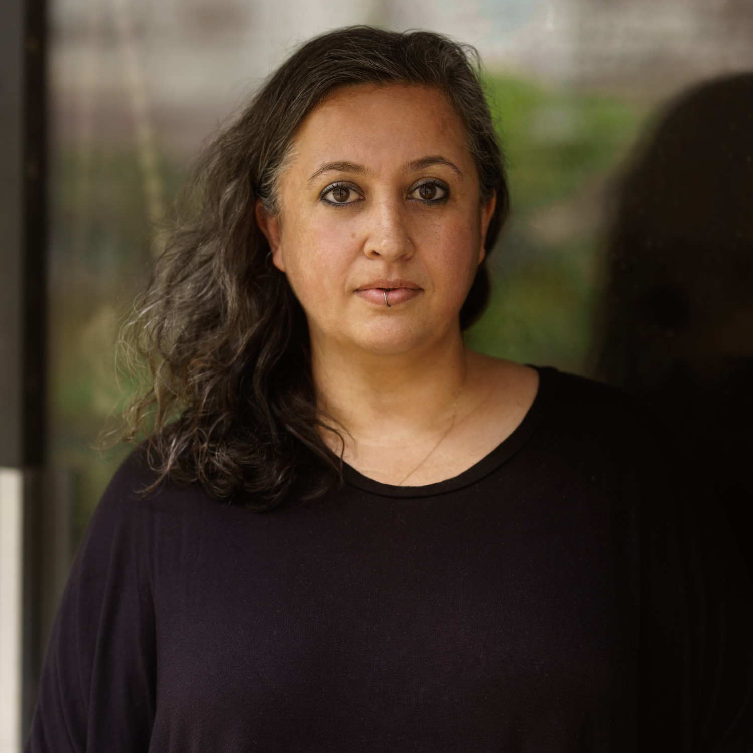 A woman with shoulder-length wavy hair and a lip ring in a black round-neck t-shirt