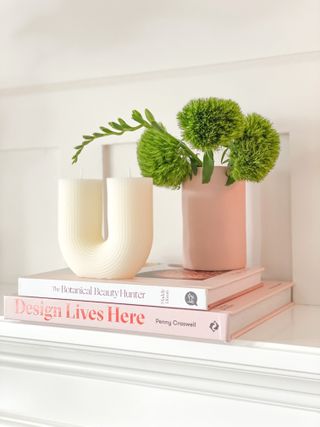 Stacked books with sculptural candle and green stems in vase.