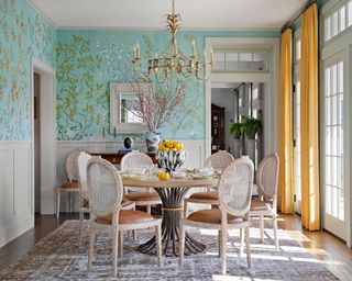 dining room with aqua patterned wallpaper, round table and cane back chairs, and yellow curtains