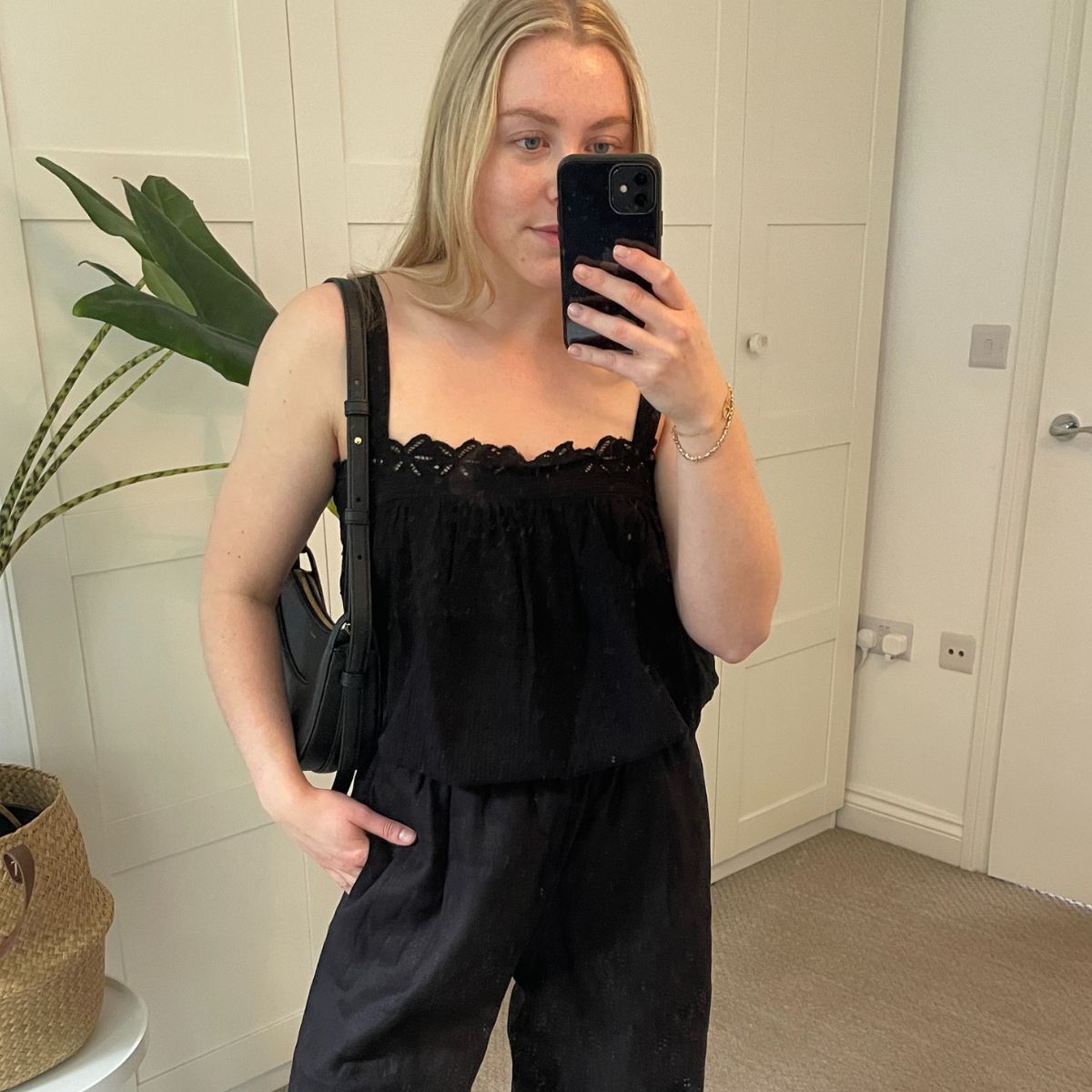 Woman wears black top, black linen trousers and black handbag