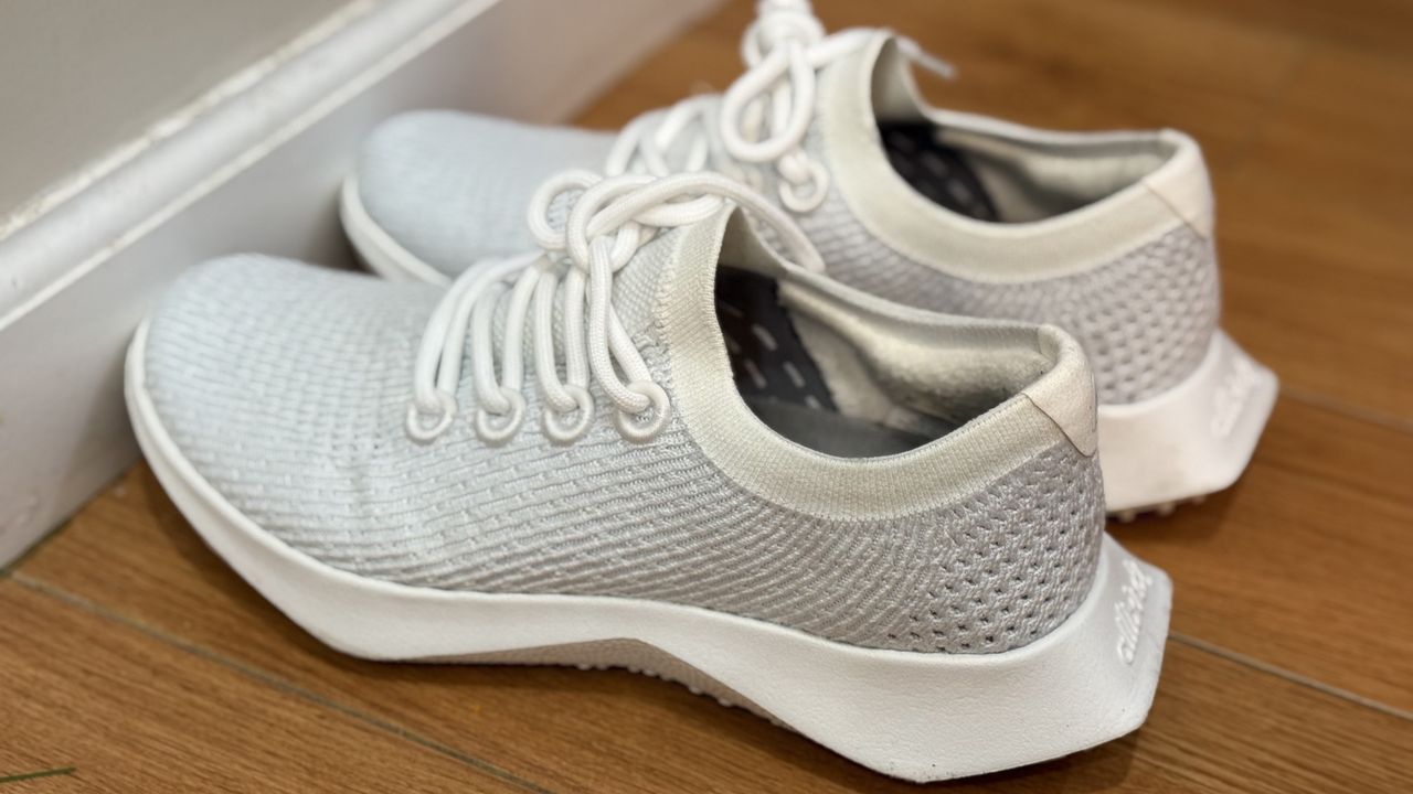 White and grey AllBirds Tree Dasher 2 sneakers on a wooden floor lined up against a white wall.