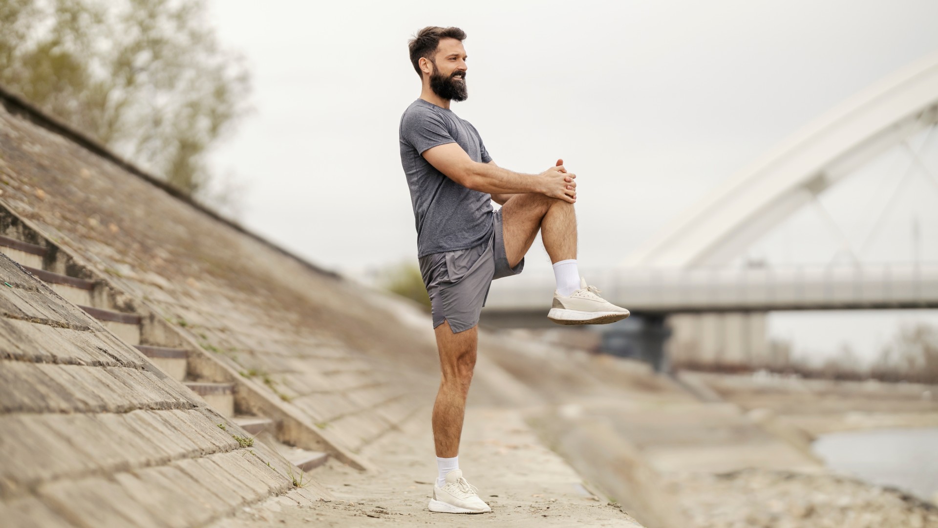 Male in shorts and t-shirt balancing on one leg while hugging his knee outdoors 