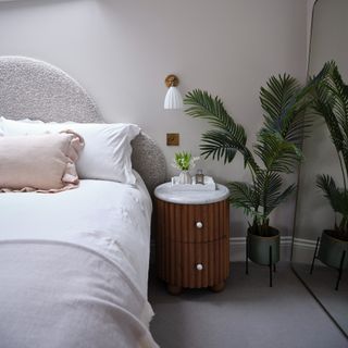 A bedroom with a bed with a boucle curved headboard and a wall light above the bedside table