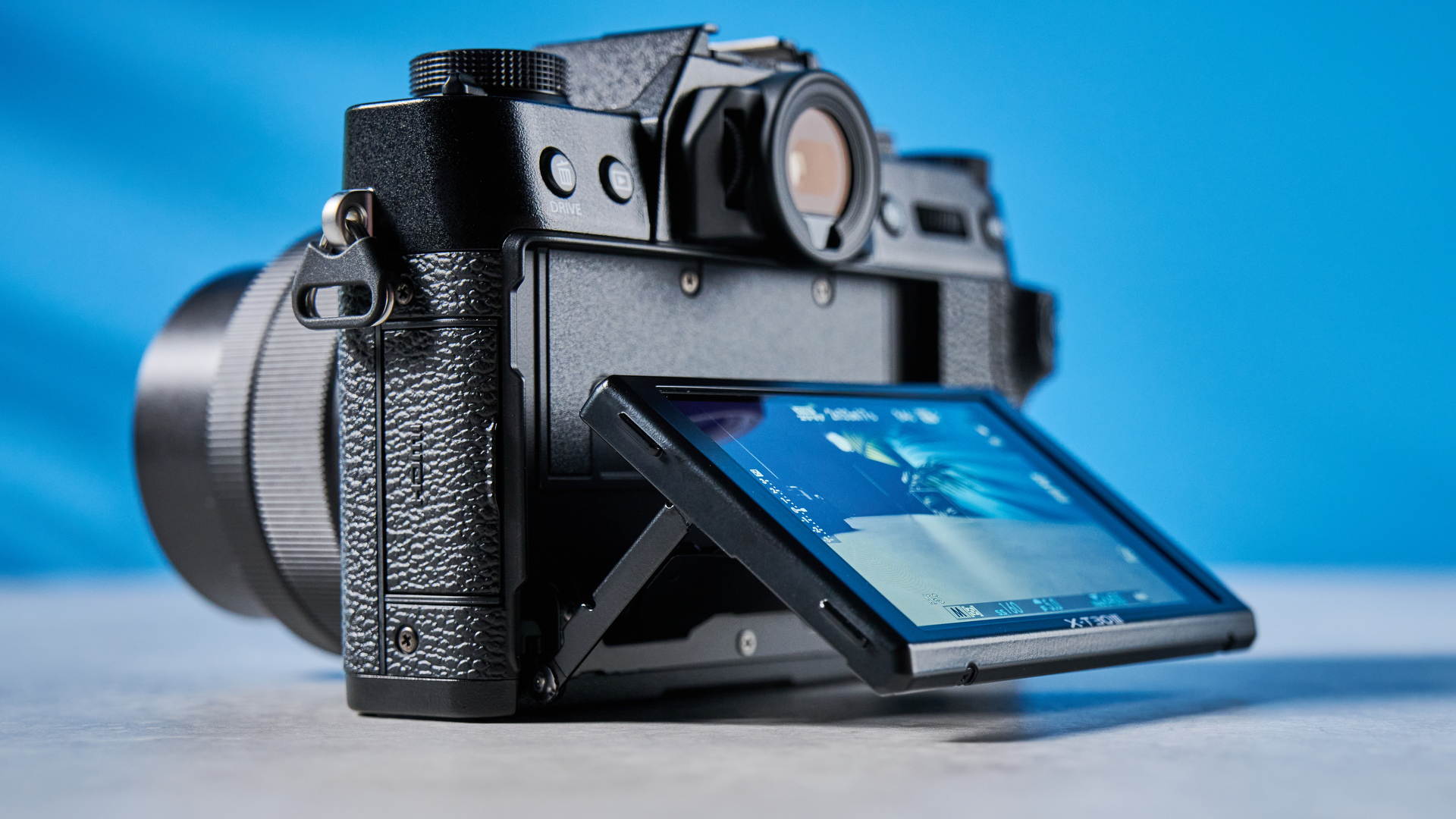 The Fujifilm X-T30 III with its display outstretched, on a stone surface with a blue background
