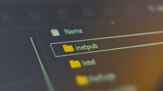 Photograph focusing on a laptop screen showing the 'inetpub' folder in Windows 11's system drive.