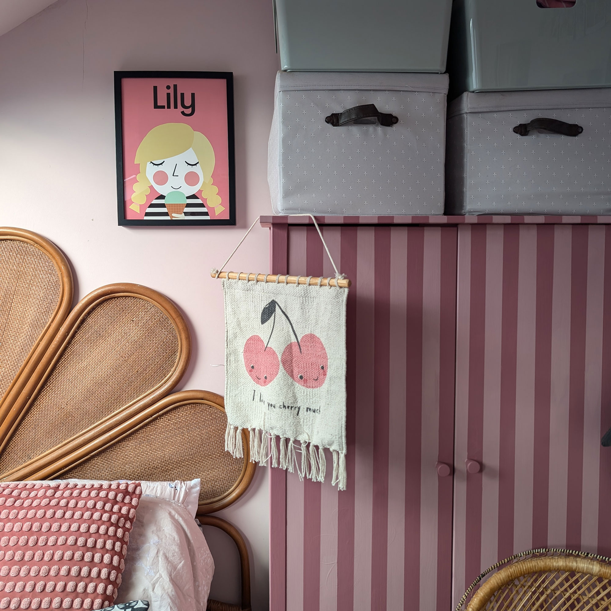 Pale pink child's bedroom with striped wardrobe, rattan headboard and artwork on walls