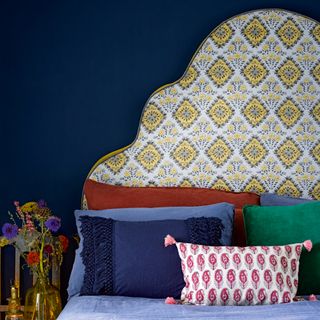 Blye bedroom with oversized, shapely headboard upholstered in patterned yellow fabric