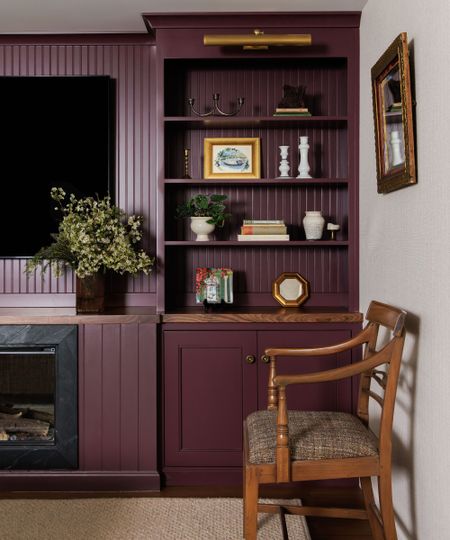 A living room with a burgundy wall and built-in shelving and cupboard, styled with decorative objects. 