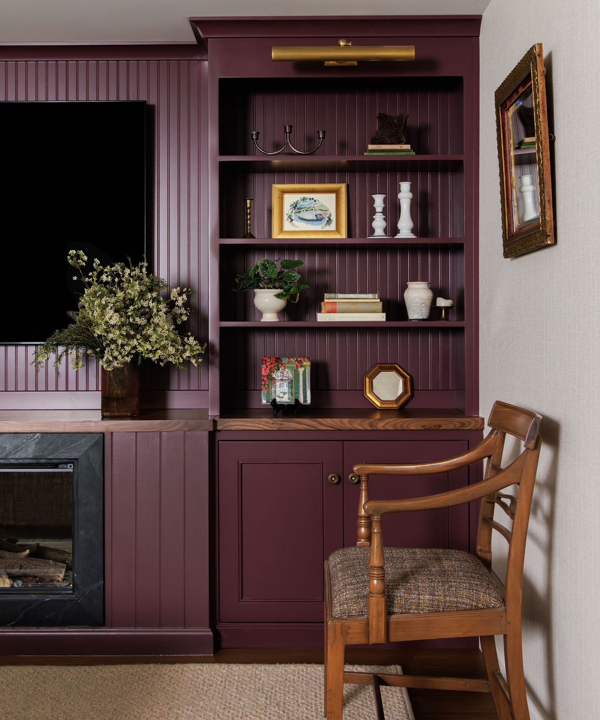 A living room with a burgundy wall and built-in shelving and cupboard, styled with decorative objects.
