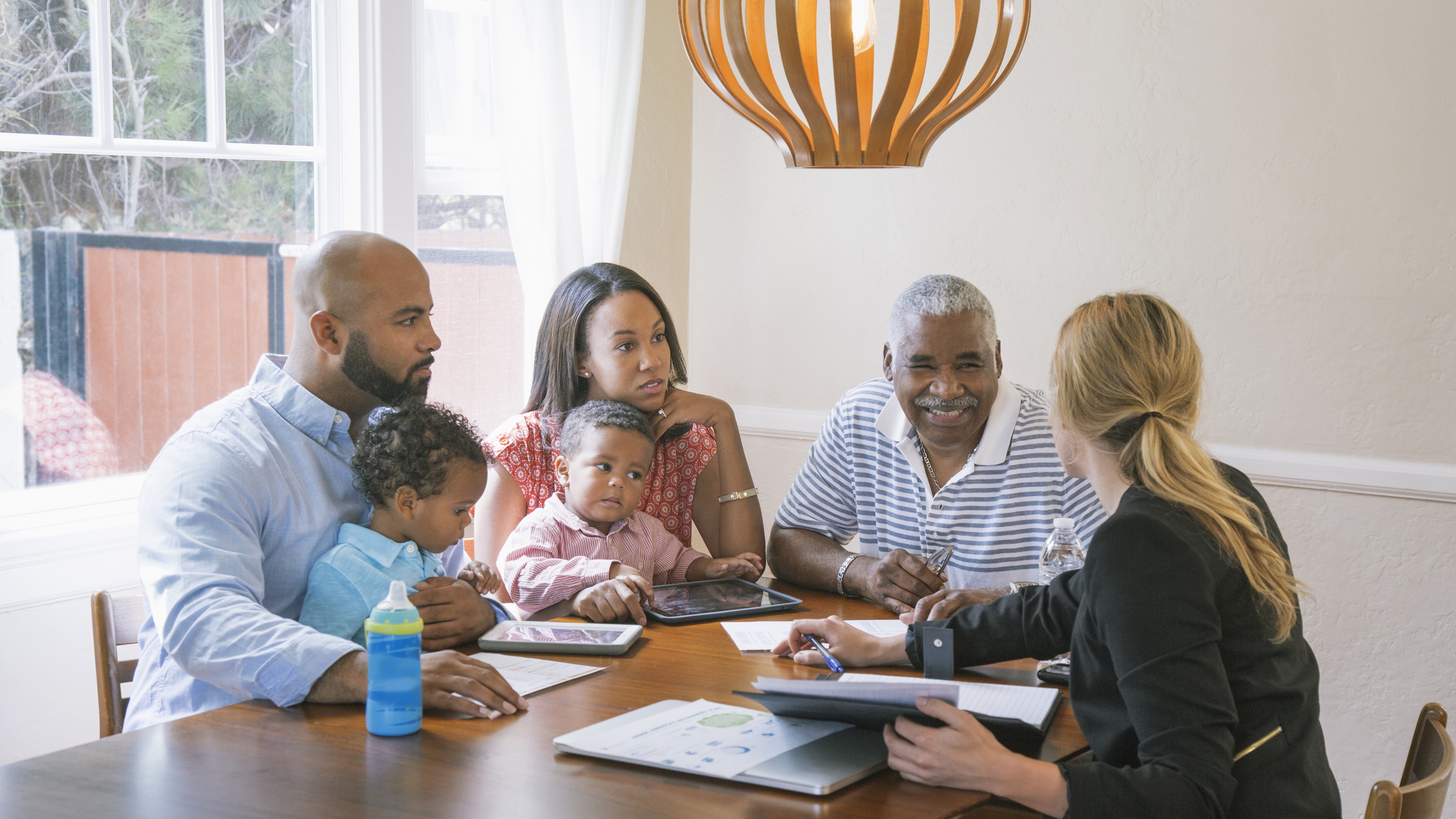 A multigenerational family talks with a financial adviser at their dining room table.