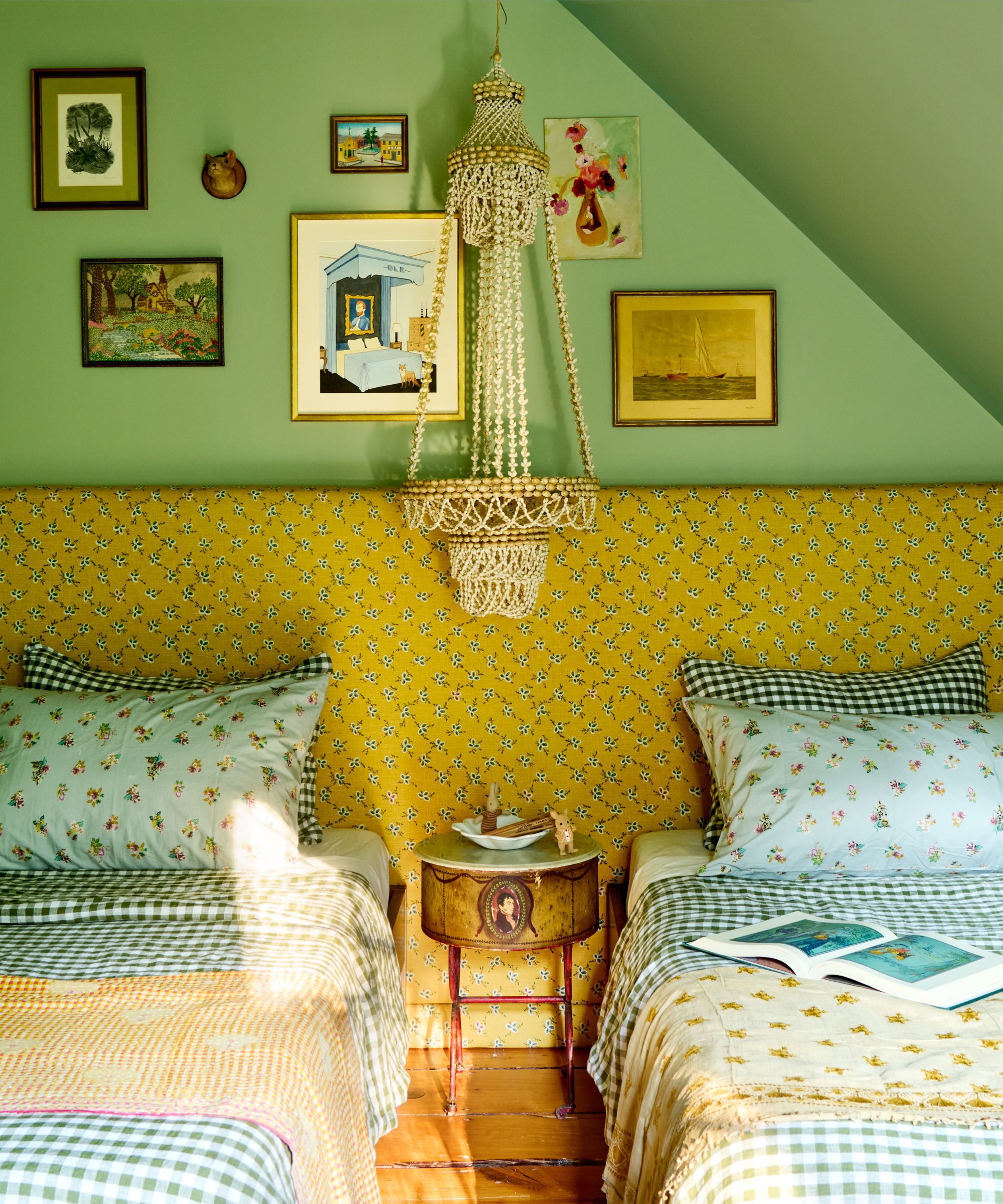 Colorful bedroom with green painted walls, patterned upholstered headboard with yellow print, two matching twin beds with gingham bedding and cushions