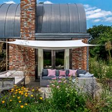 A brick building with a shade sail extending out over an outdoor sofa