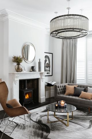 white living room with marble fire surround and ochre chair and cushions, grey sofa, grey curtains, big chandelier