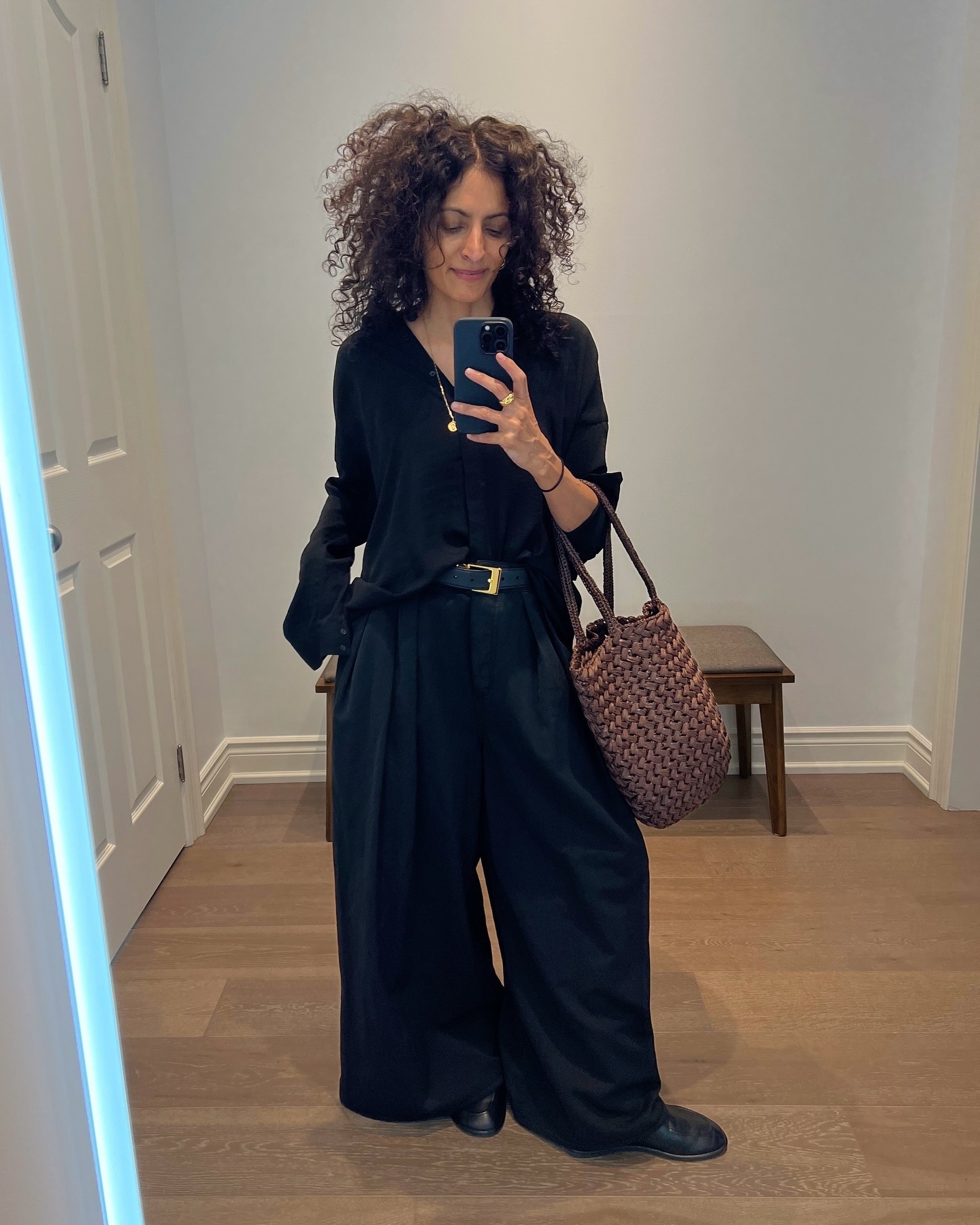 Woman wears black shirt black trousers, black loafers and carries brown woven tote