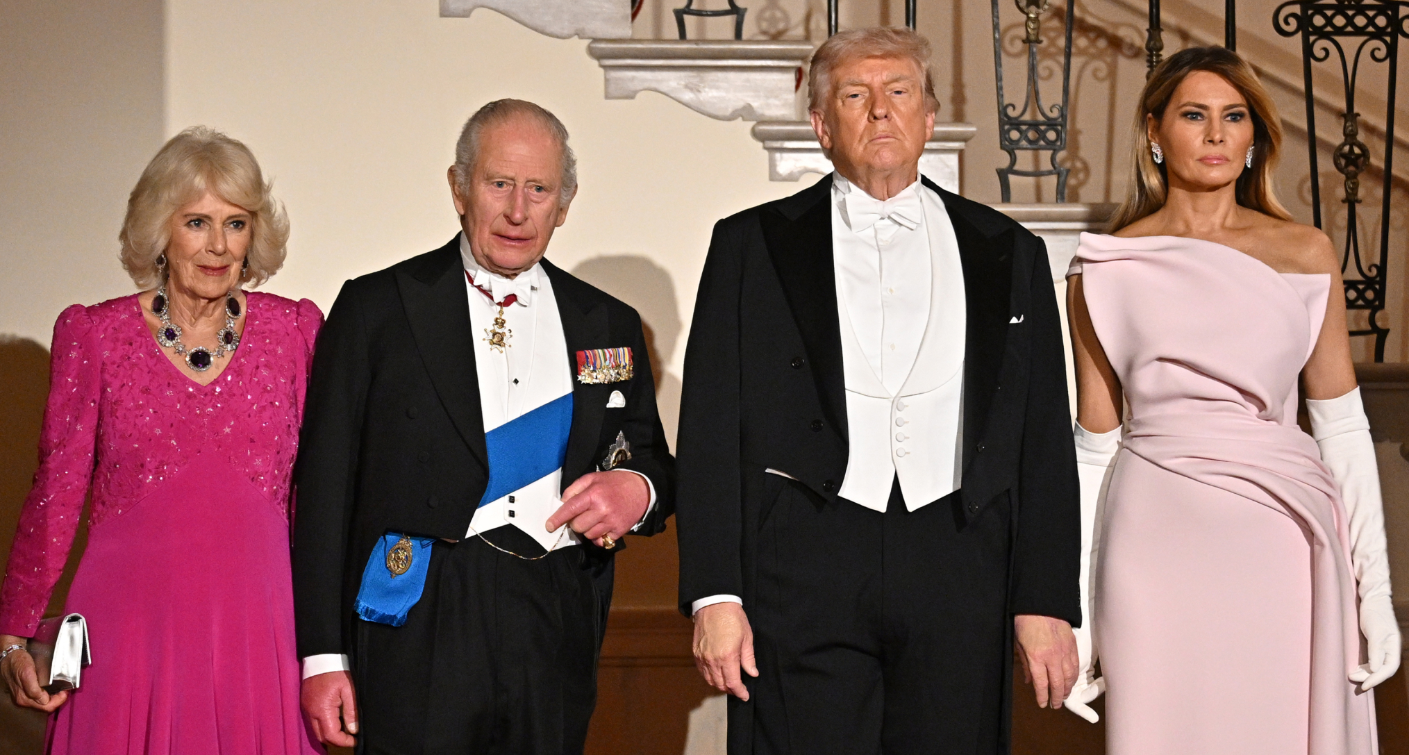 Queen Camilla in a pink gown and amethyst necklace standing next to King Charles, Donald and Melania Trump 