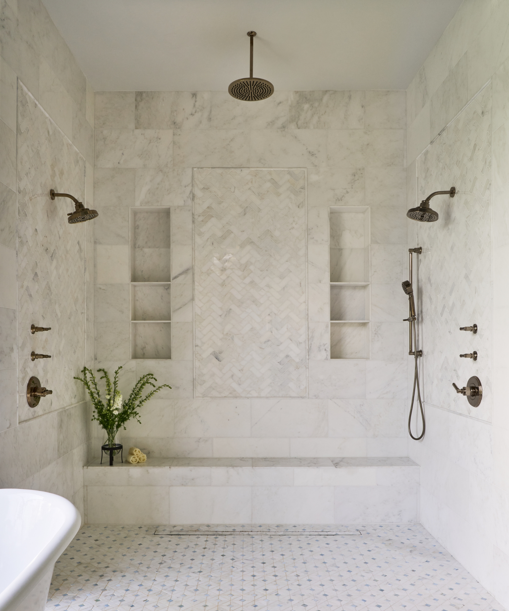 A white wet room with recessed niche storage, three shower heads, and a freestanding bath