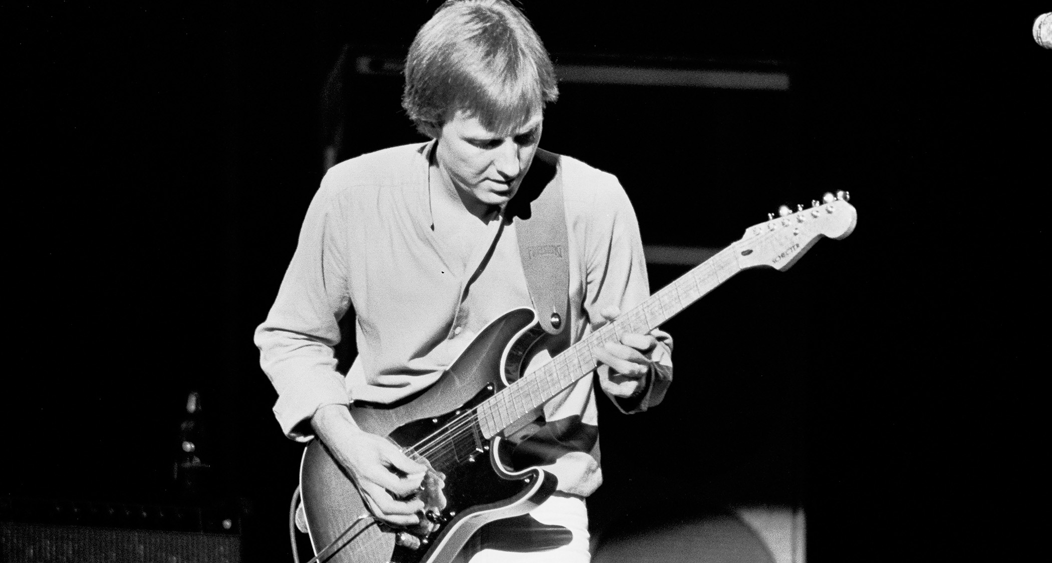 A black-and-white shot of legendary English guitarist Clem Clempson playing a Schecter S-style onstage in 1980.