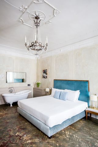 Guest room featuring blue headboard, free-standing bath and chandelier