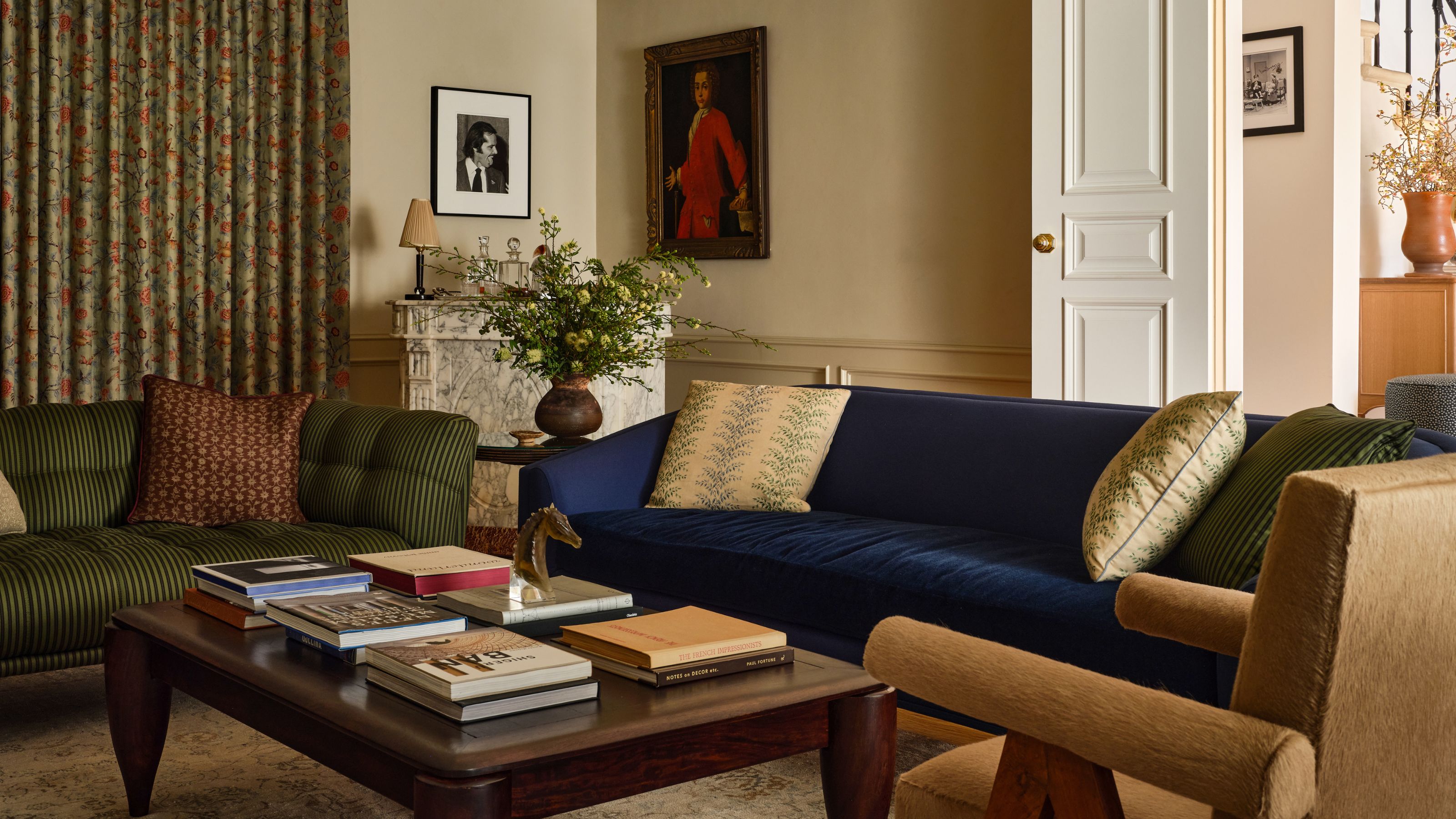 Cozy living room with a navy velvet sofa, a striped olive green sofa, an orange upholstered armchair, and a dark wood coffee table in front of a marble fireplace