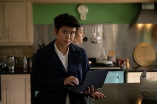 DC Blair Ferguson (Katie Leung) stands in a kitchen, typing on a laptop computer that she's holding with her other hand