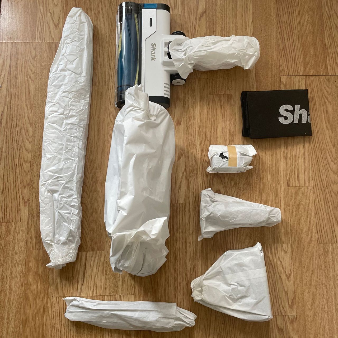 Shark PowerPro Pet Cordless Stick Vacuum components wrapped in paper, laying on laminate flooring